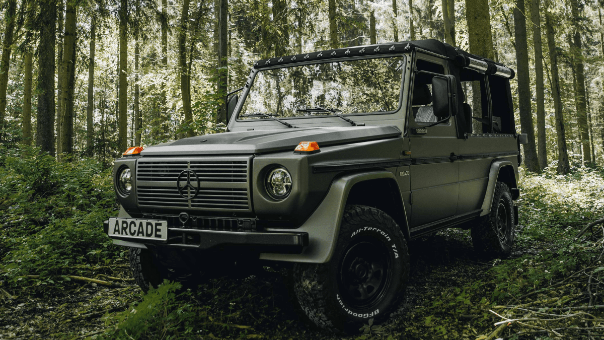 Modified and customized matte green Classic Mercedes-Benz GE 230 parked in a forest background.